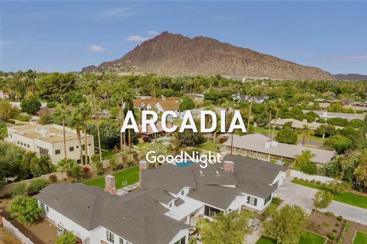 A peaceful neighborhood scene with a sprawling green lawn, residential homes nestled in lush greenery, and a backdrop of stunning mountain ranges. The spacious lawn and clear skies evoke a sense of tranquility and ample outdoor space for relaxation or recreation.