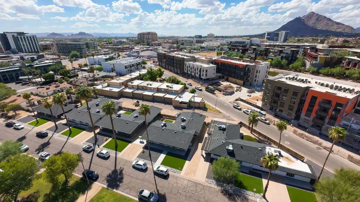 A vibrant exterior shot featuring modern apartment buildings bordered by palm trees and open green spaces, all set against the dramatic backdrop of nearby mountains. The energetic atmosphere invites group gatherings and exploration of the surrounding urban area.