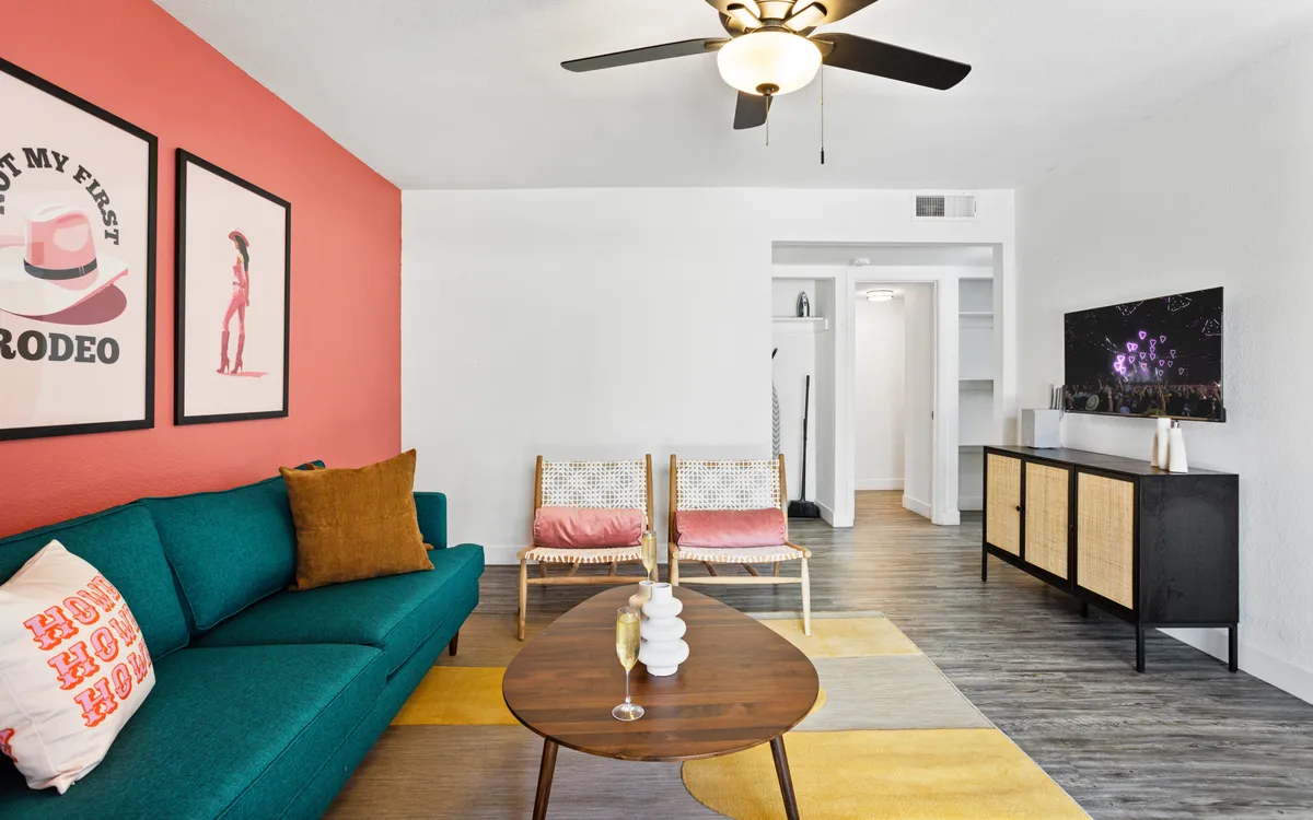 A playful and cozy living room featuring a turquoise sofa, vibrant wall art, a modern wooden coffee table, woven chairs, and a TV unit. The space is designed for both relaxation and socializing, hinting at opportunities for movie marathons and group activities.
