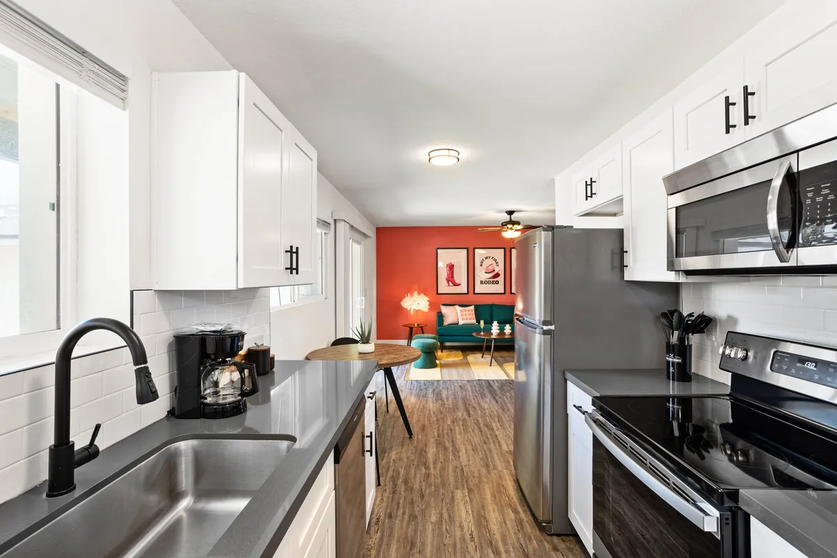 This image highlights a vibrant, modern kitchen space featuring up-to-date appliances, a striking red accent wall, comfortable seating, and decorative wall art. The room’s design signals a welcoming area perfect for preparing meals and social gatherings.
