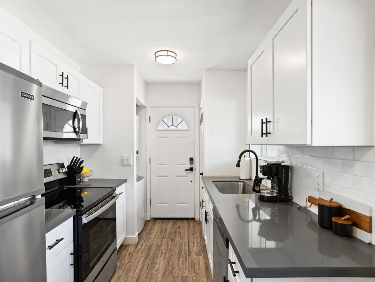 A sleek kitchen with stainless steel appliances, crisp white cabinetry, a convenient countertop coffee maker, and a wooden cutting board. The overall look is fresh, functional, and well-equipped for both big meals and quick breakfasts.